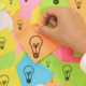 Sticky notes with light bulbs and a hand sticking one on the board