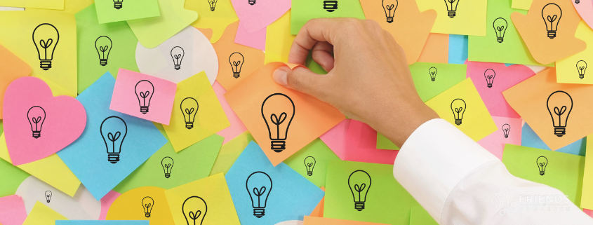 Sticky notes with light bulbs and a hand sticking one on the board